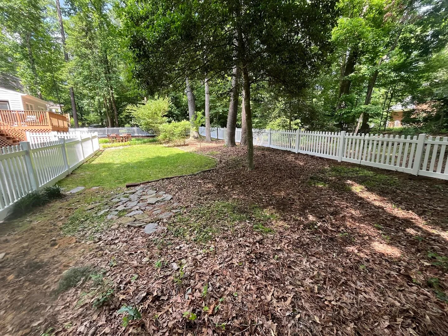 White picket fence surrounding a green backyard, showing eco-friendly fencing materials that blend with natural landscapes.